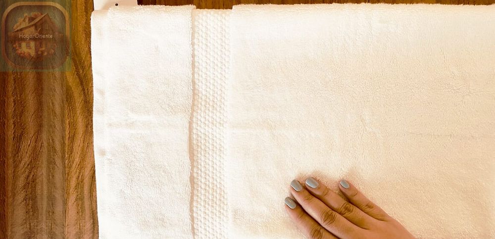mano doblando una toalla blanca grande sobre una mesa de madera